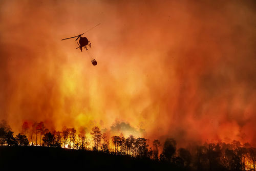 Helicopter dropping water on large forest fire.