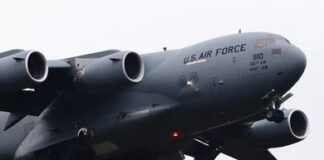 Military aircraft unloading vehicles at an airport with security personnel present