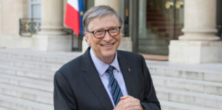 Man in suit outside building, flag in background.