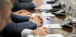 Business meeting participants with hands clasped at a conference table with microphones