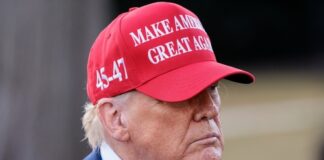 A man wearing a red cap with a political slogan, looking serious