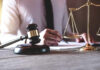 Gavel and scales beside a person writing.