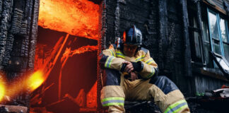 Firefighter resting near a burned-out building.
