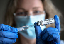 COVID Vaccine Shield Ending? Person holding COVID-19 vaccine vial and syringe.