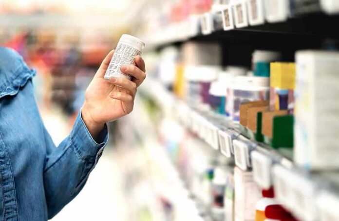 shutterstock_1328838881 Shopper holding a pill bottle in a pharmacy aisle