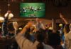 Crowd cheering in a sports bar while watching a football game on a large screen