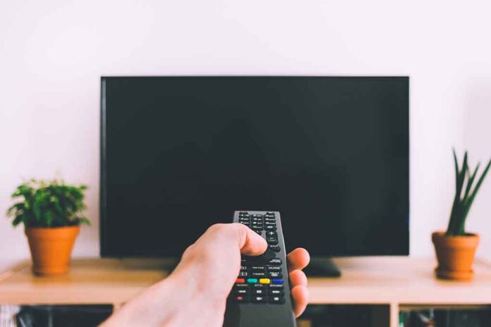 Hand holding remote towards blank TV screen.