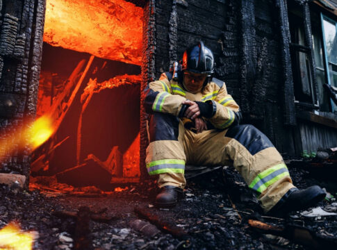 Firefighter resting near a burned-out building.