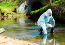 Person in protective gear collecting water sample from stream.