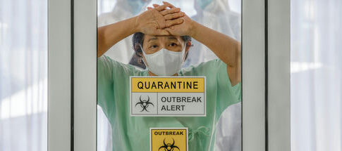 A healthcare worker in a green uniform and mask, looking distressed behind a glass door marked with quarantine signs