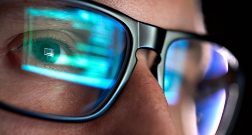 Man with glasses reflecting computer code screen.