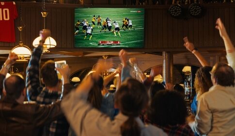Crowd cheering in a sports bar while watching a football game on a large screen