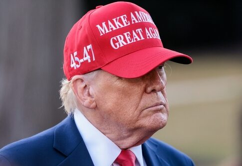 A man wearing a red cap with a political slogan, looking serious