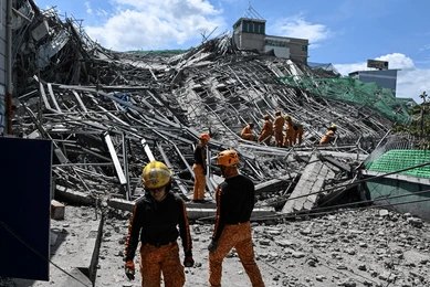 People walk through a street of destroyed buildings and rubble